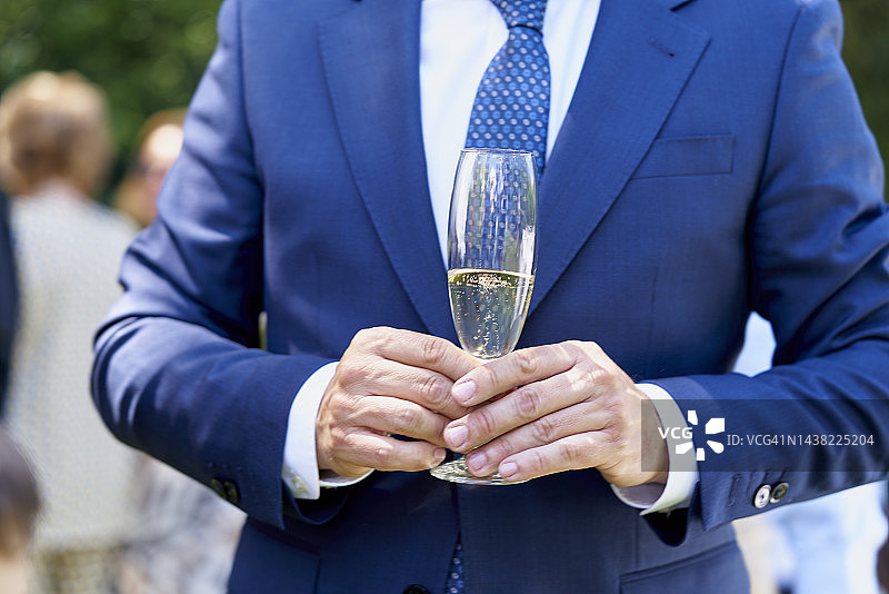 特写：男子在社交庆典中身穿蓝色西装，手持香槟酒杯图片素材