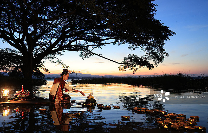 穿着泰国传统服装的亚洲女性手捧水灯，在泰国水灯节放水灯。每年11月举行的水灯节是为了祈求对水神的尊重图片素材