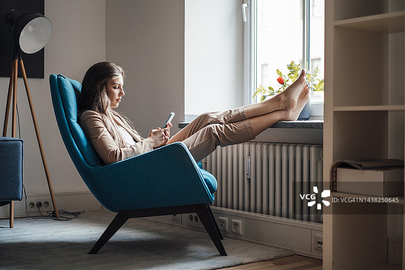 女商人坐在家里的椅子上用智能手机图片素材