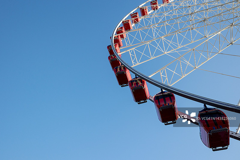 晴朗蓝天下摩天轮的白色结构和红色舱体图片素材