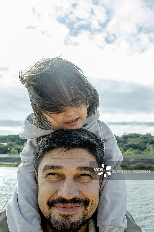 在河边肩上扛着儿子的微笑父亲图片素材