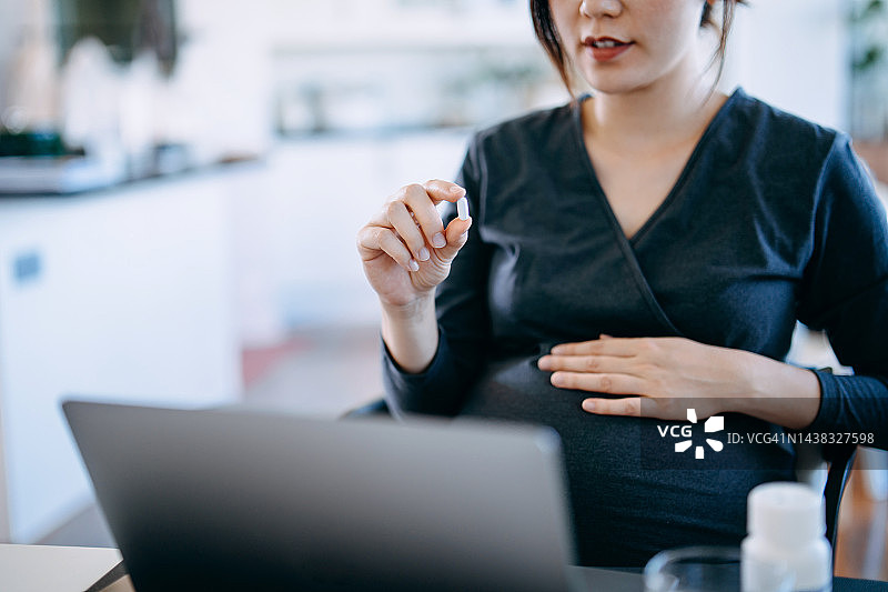 年轻亚裔孕妇在家用笔记本电脑与医生进行视频通话，咨询用药图片素材