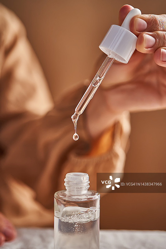 穿着米色连衣裙的女孩手拿滴管滴精华液图片素材