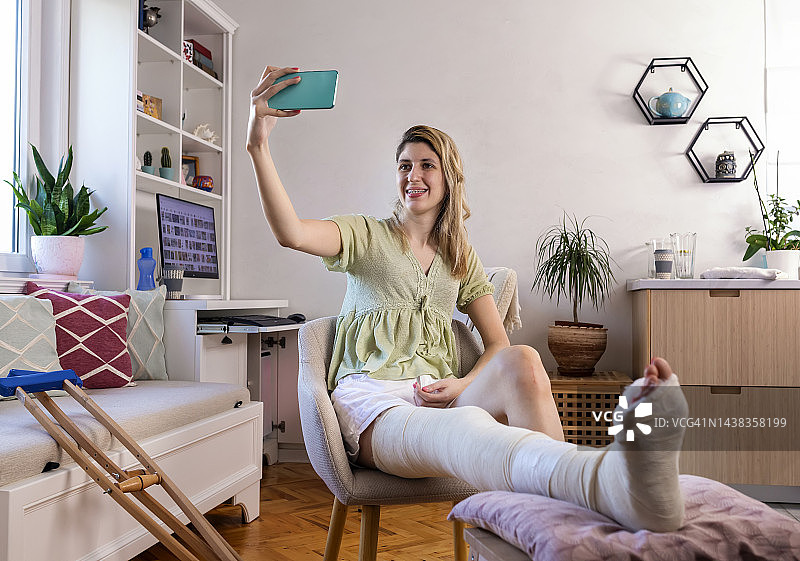 腿部打着石膏的年轻女人正在使用手机图片素材