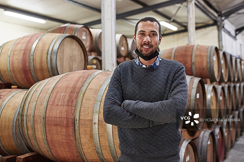新冠、葡萄酒和农场，一名男子在地窖里酿造葡萄酒，从事农业生产。可持续性、农业和木桶，男农民在仓库里图片素材