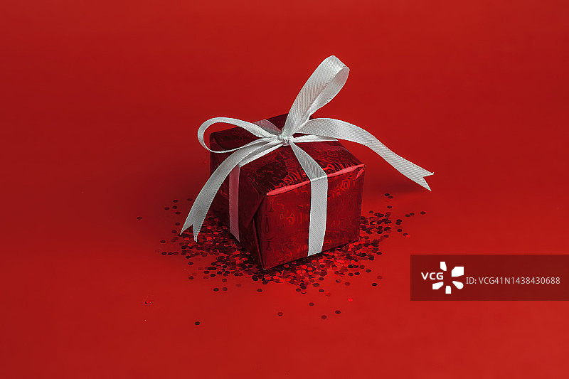 红色背景上带有白色蝴蝶结和闪亮装饰的礼品盒，盈利概念图片素材