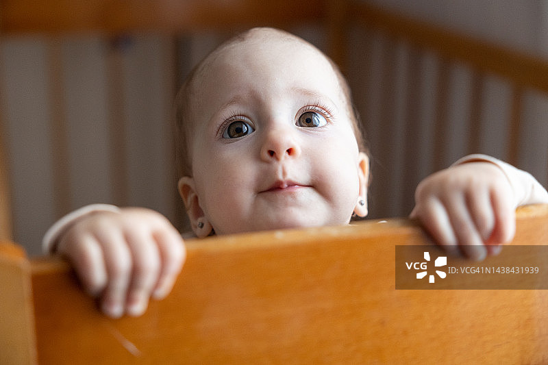 站在婴儿床边抓住木制栏杆的女婴图片素材