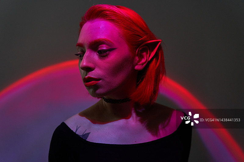 拥有红色头发和精灵耳朵的年轻漂亮女人，红紫色灯光，数字时代未来概念图片素材