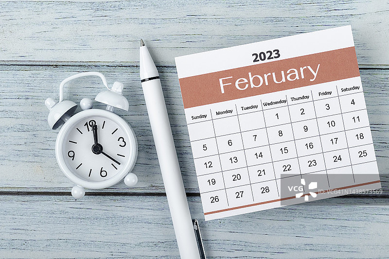 2023年台历：二月是计划和截止日期月，背景为木桌上的闹钟和白色笔图片素材