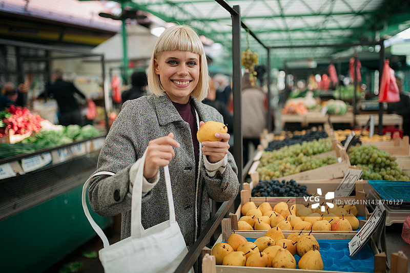 快乐的年轻女子在农贸市场购买梨图片素材
