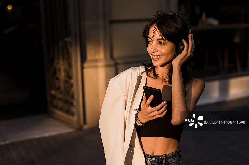 一位年轻的西班牙妇女走在城市的街道上，用无线耳机听着音乐，用着手机图片素材