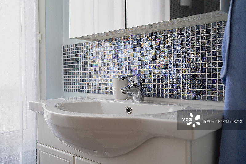 浴室：带金属水龙头的水槽，瓷砖墙壁旁边的窗户在白天拉着窗帘图片素材