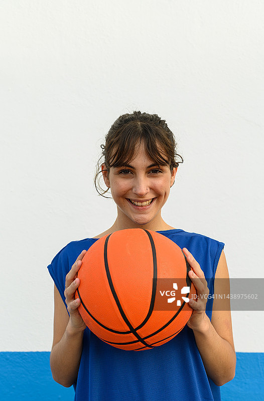 手持篮球，笑容灿烂的篮球女运动员，蓝白背景图片素材