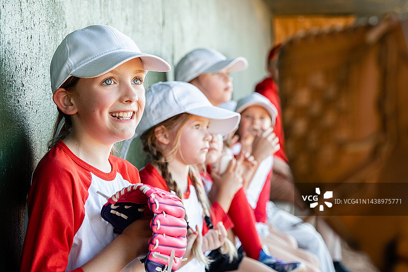 穿着制服戴着棒球手套的小女孩坐在小联盟球队的休息区里图片素材