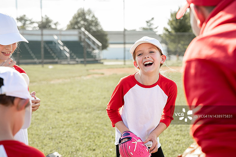 可爱的小女孩在少儿棒球比赛中与队友交谈时微笑图片素材