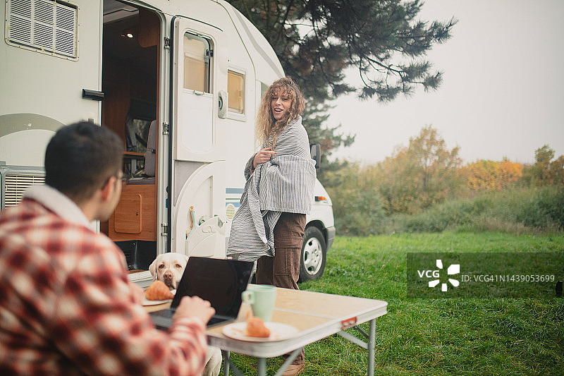 一位快乐的女子与男友一起露营，她的男友使用笔记本电脑进行远程工作图片素材
