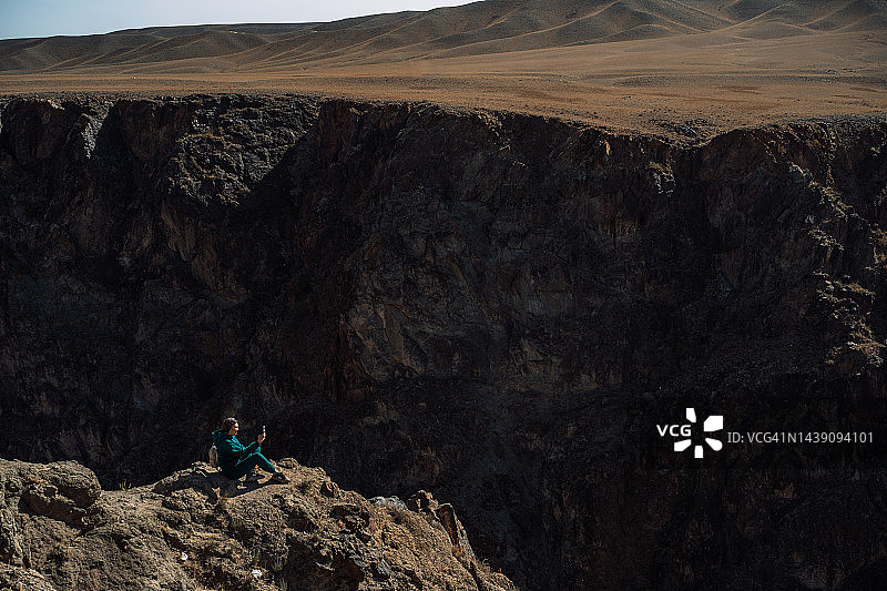 身穿绿色套装坐在高峡谷上的女人图片素材
