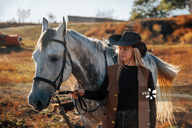 身穿牛仔服的女人牵着马，拿着缰绳图片素材