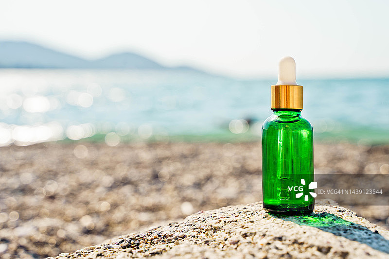 绿色面部精华液瓶，鹅卵石背景，模糊海景图片素材