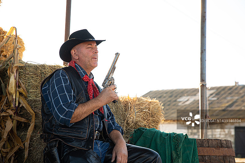 牛仔手持左轮手枪坐在木桶上图片素材