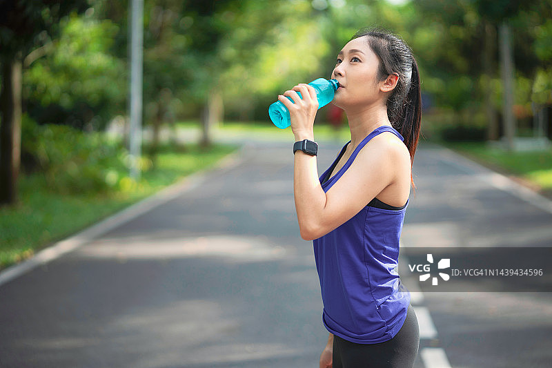 在公园跑步的年轻健身运动女性。跑步后喝水的年轻女人。在阳光明媚的日子里在户外喝水的运动型女人。图片素材