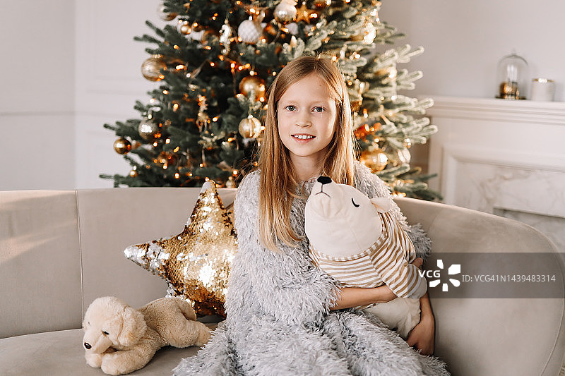 圣诞节拍摄概念：少女在装饰过的房间里手持礼物和玩具坐在沙发上图片素材