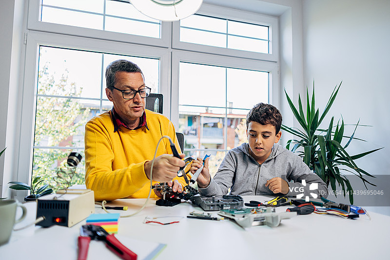 儿子帮助父亲焊接电子设备的组件图片素材