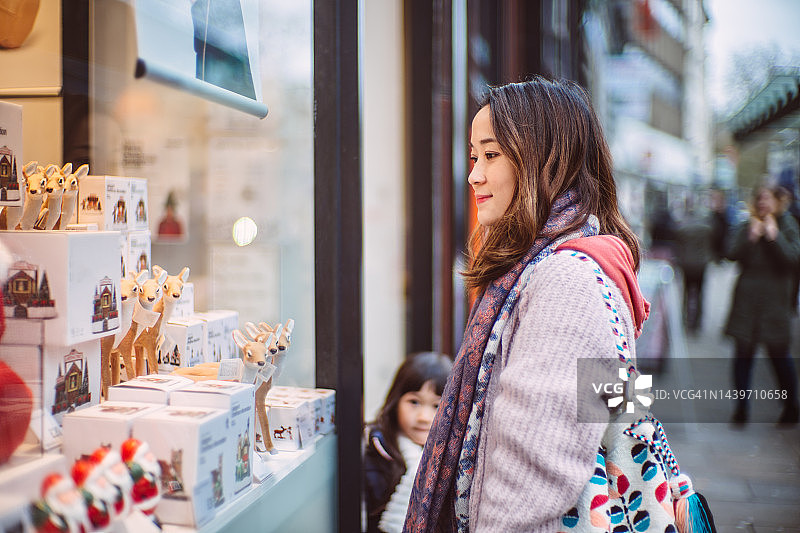 年轻漂亮的妈妈和可爱的女儿在市中心区看着商店橱窗里的圣诞节装饰品图片素材