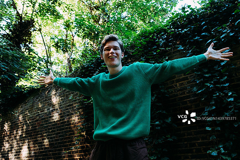 青年男子在砖墙前张开双臂图片素材