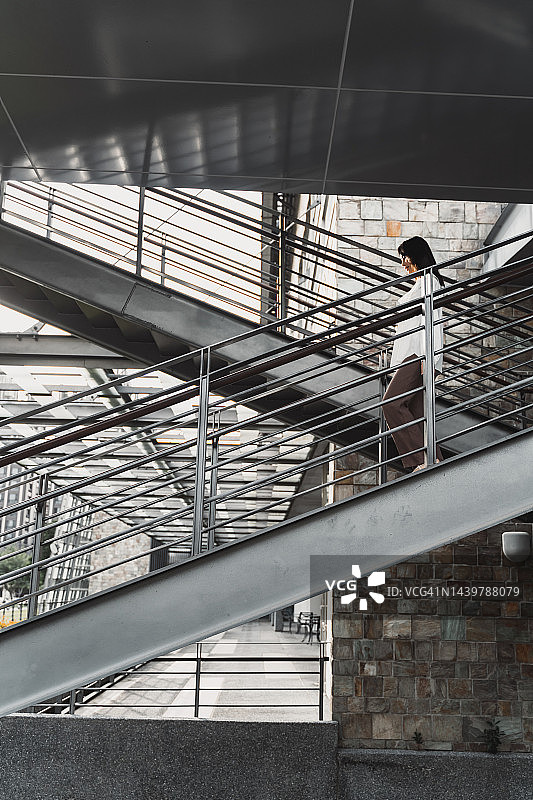 年轻的亚洲女人使用移动设备走下室外楼梯图片素材