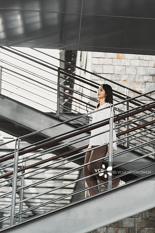 年轻的亚洲女人使用移动设备走下室外楼梯图片素材