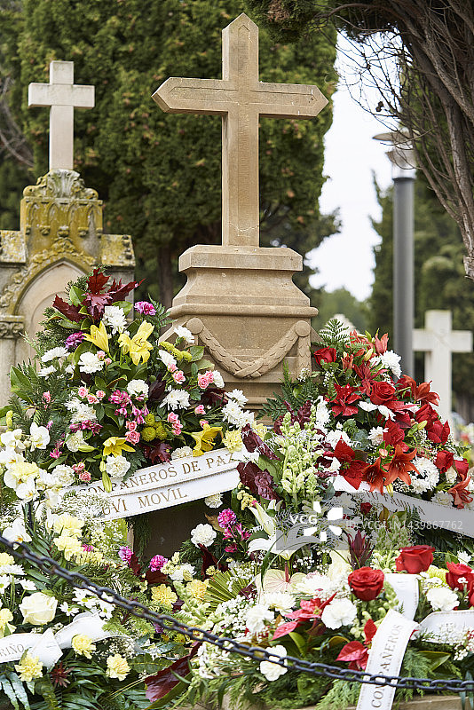 十字形墓碑上玫瑰和其他花朵的插花，花上写着文字，正面图片素材