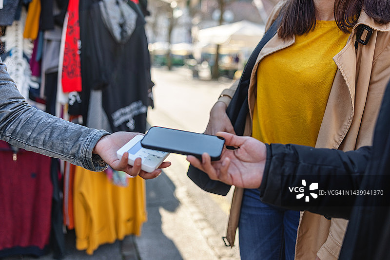 朋友们在街头市场摊位上用智能手机支付服装费用图片素材