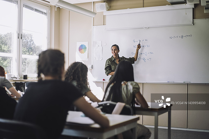 微笑的老师在教室里向女学生讲解数学公式图片素材