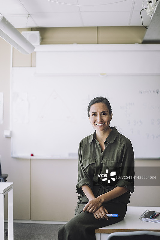 坐在学校教室桌子旁微笑的女教师肖像图片素材