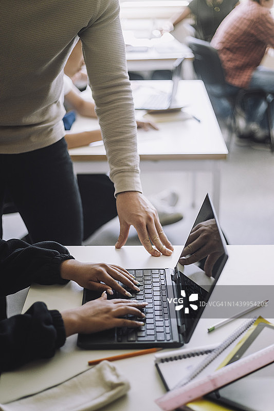 在学校教室里，女孩在教授的指导下使用笔记本电脑的局部图像图片素材