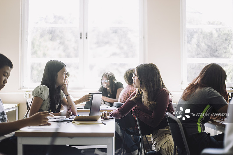 在学校教室里一边电子学习一边讨论的初中生图片素材