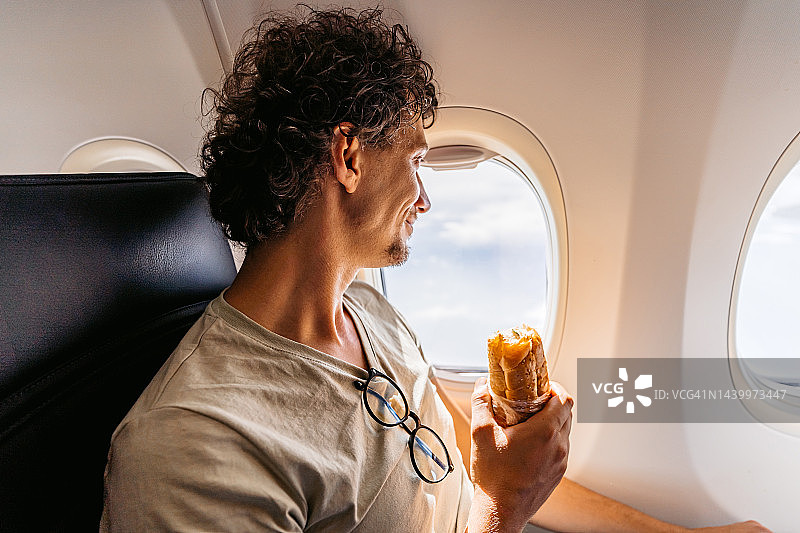 在飞机上吃三明治的年轻男人图片素材