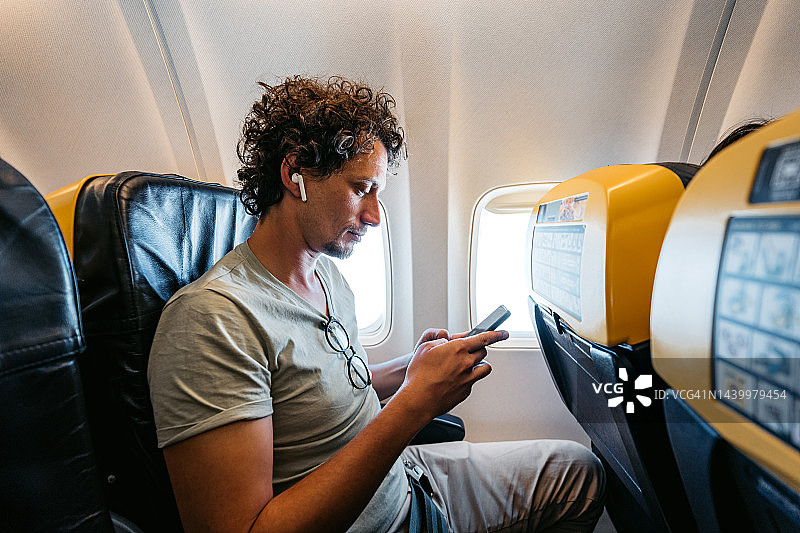 在飞机上使用智能手机的年轻男人图片素材