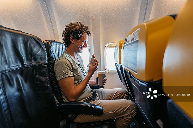 在飞机上吃三明治喝咖啡的年轻男人图片素材