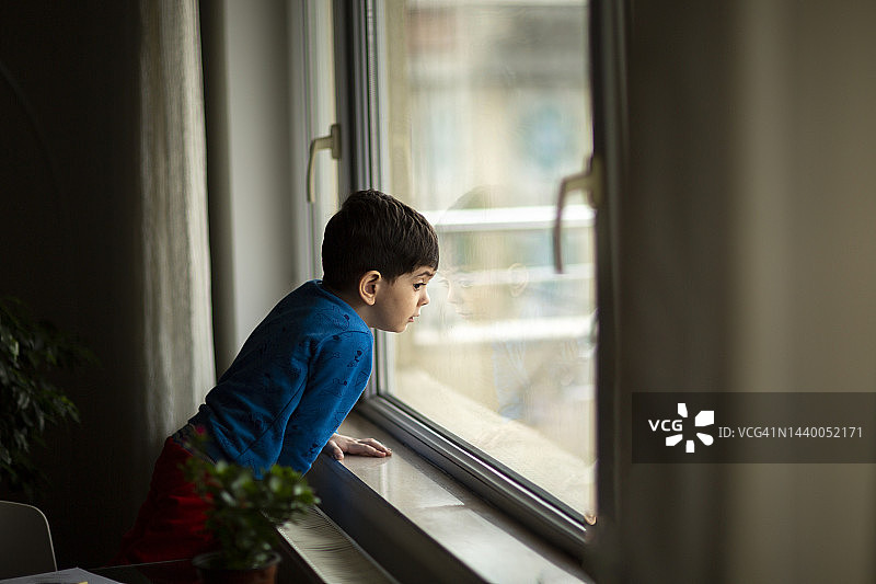 在家透过窗户等待妈妈回家的男孩图片素材