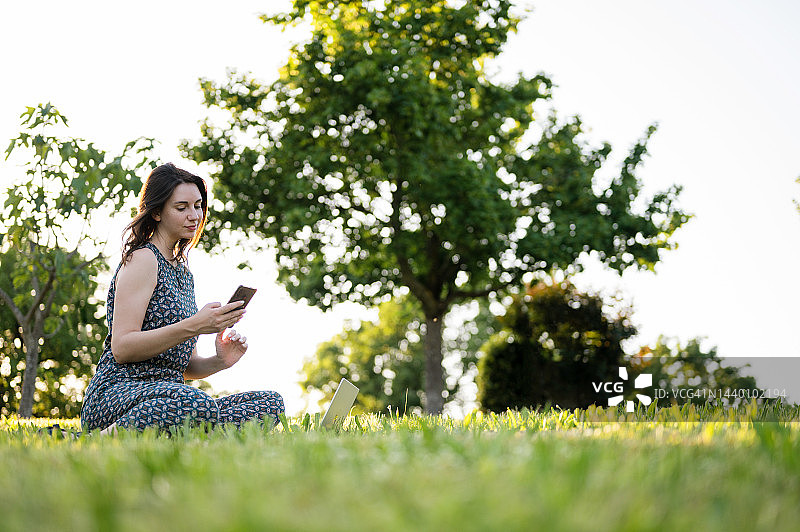 坐在公园绿草地上的迷人黑发年轻女子肖像图片素材