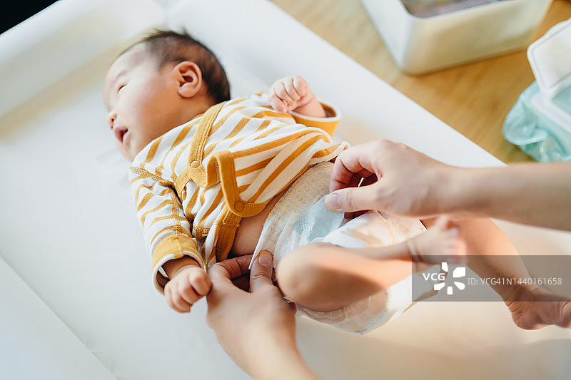 可爱的女婴躺在更换垫上，妈妈在家给她换尿布。新生活，爱，关怀和温柔图片素材