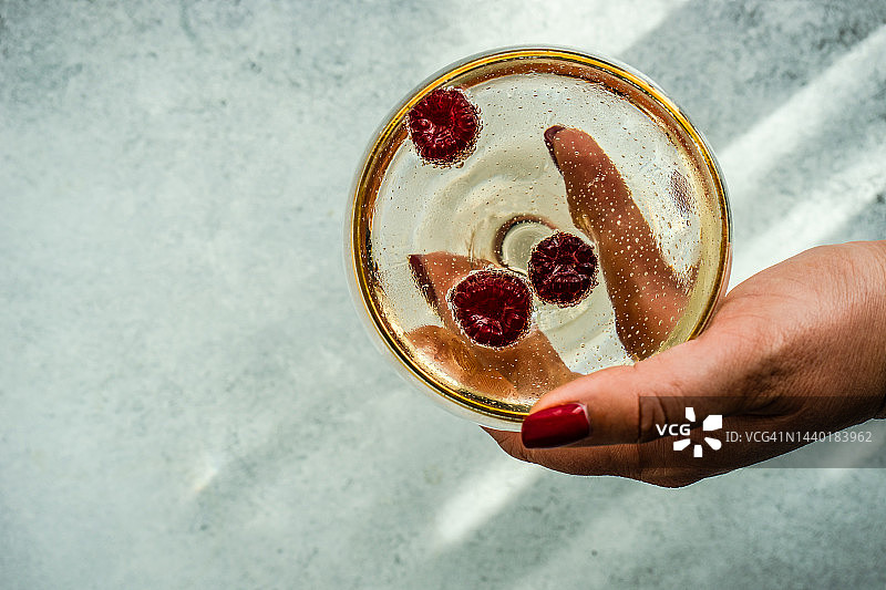 女人手持香槟杯和新鲜覆盆子俯视图片素材