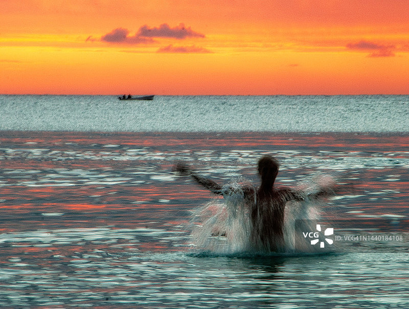 日落时分在印度洋中戏水的男子轮廓，远处有一艘船，毛里求斯图片素材