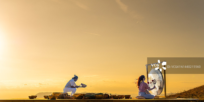 声音疗法，男人和女人在日落时演奏铜锣图片素材