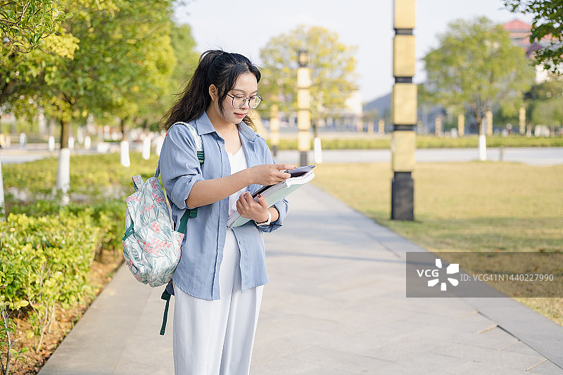 年轻女大学生站在校园里使用平板电脑。图片素材