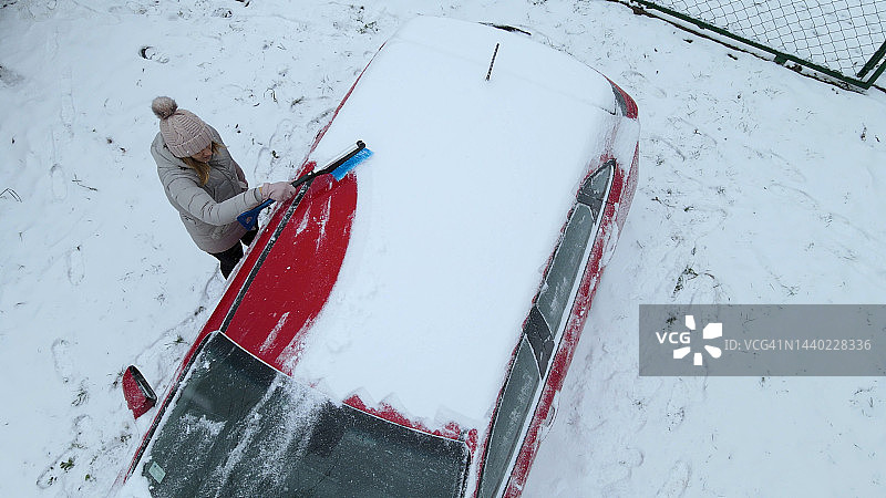 冬季早晨，女人清理汽车上的积雪图片素材