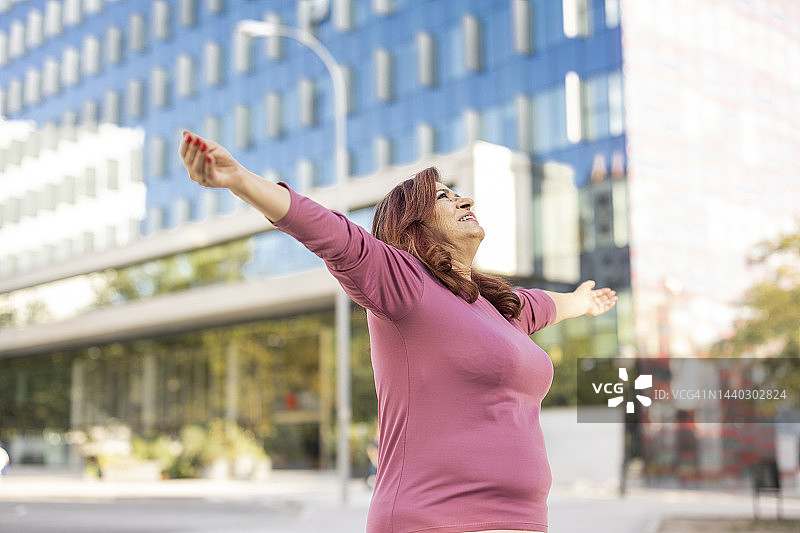 张开双臂享受城市孤独的红发年长女性图片素材