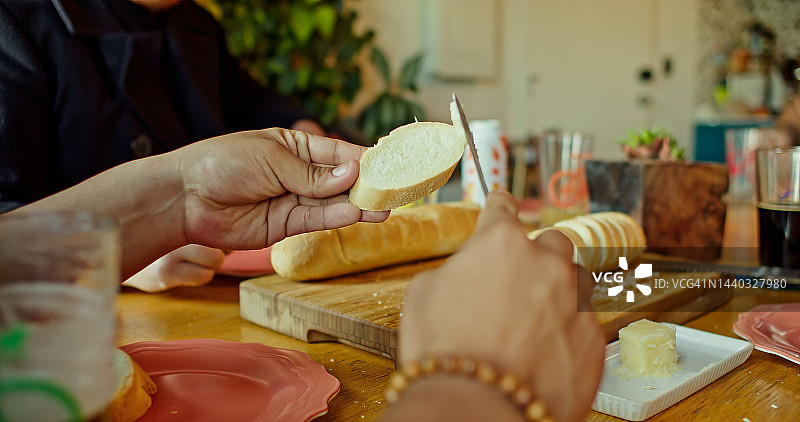 男子在餐桌旁的面包片上涂抹黄油图片素材
